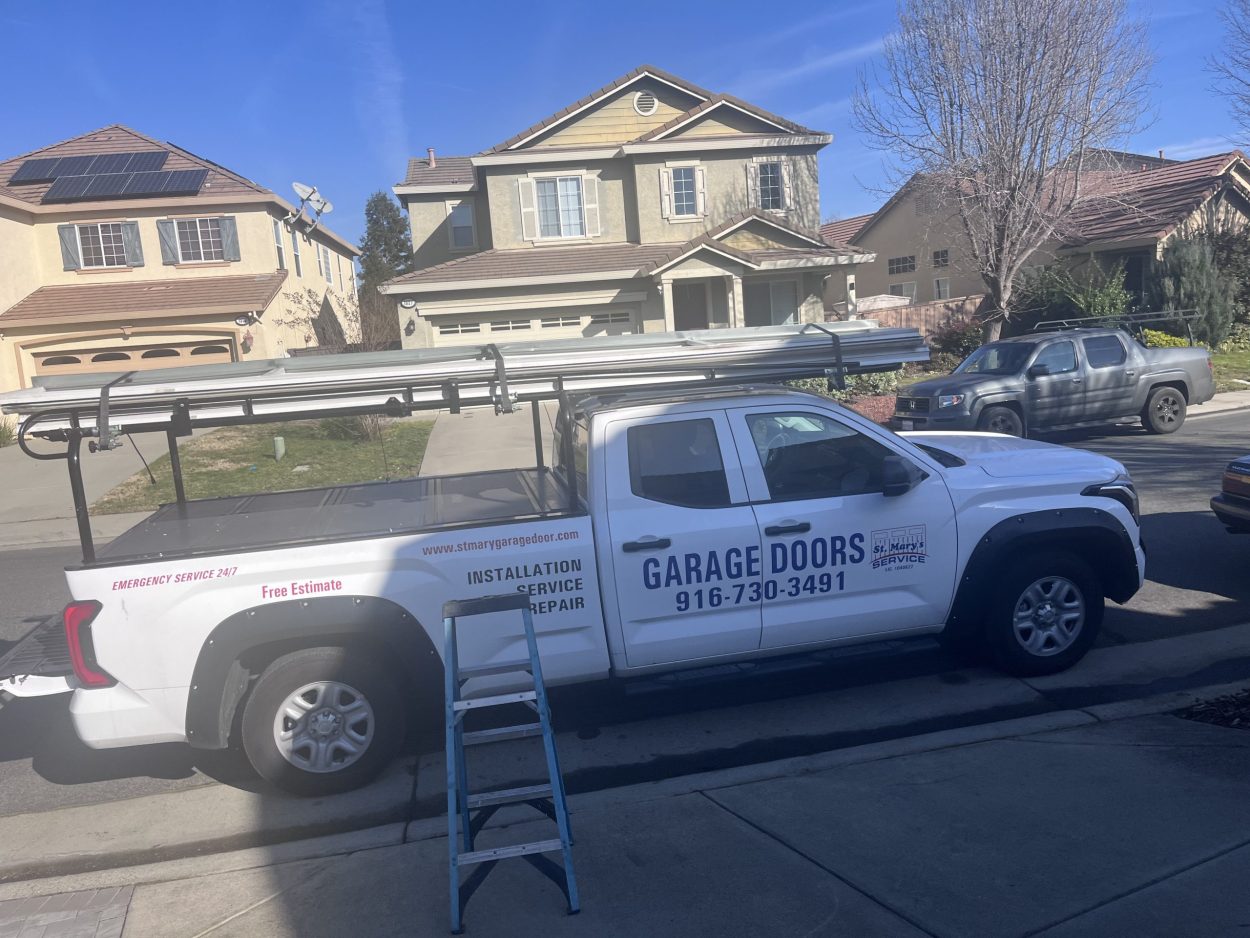 A St. Mary’s Garage Door Services truck parked in a Roseville neighborhood during a residential installation. The truck features contact info for 24/7 emergency repairs
